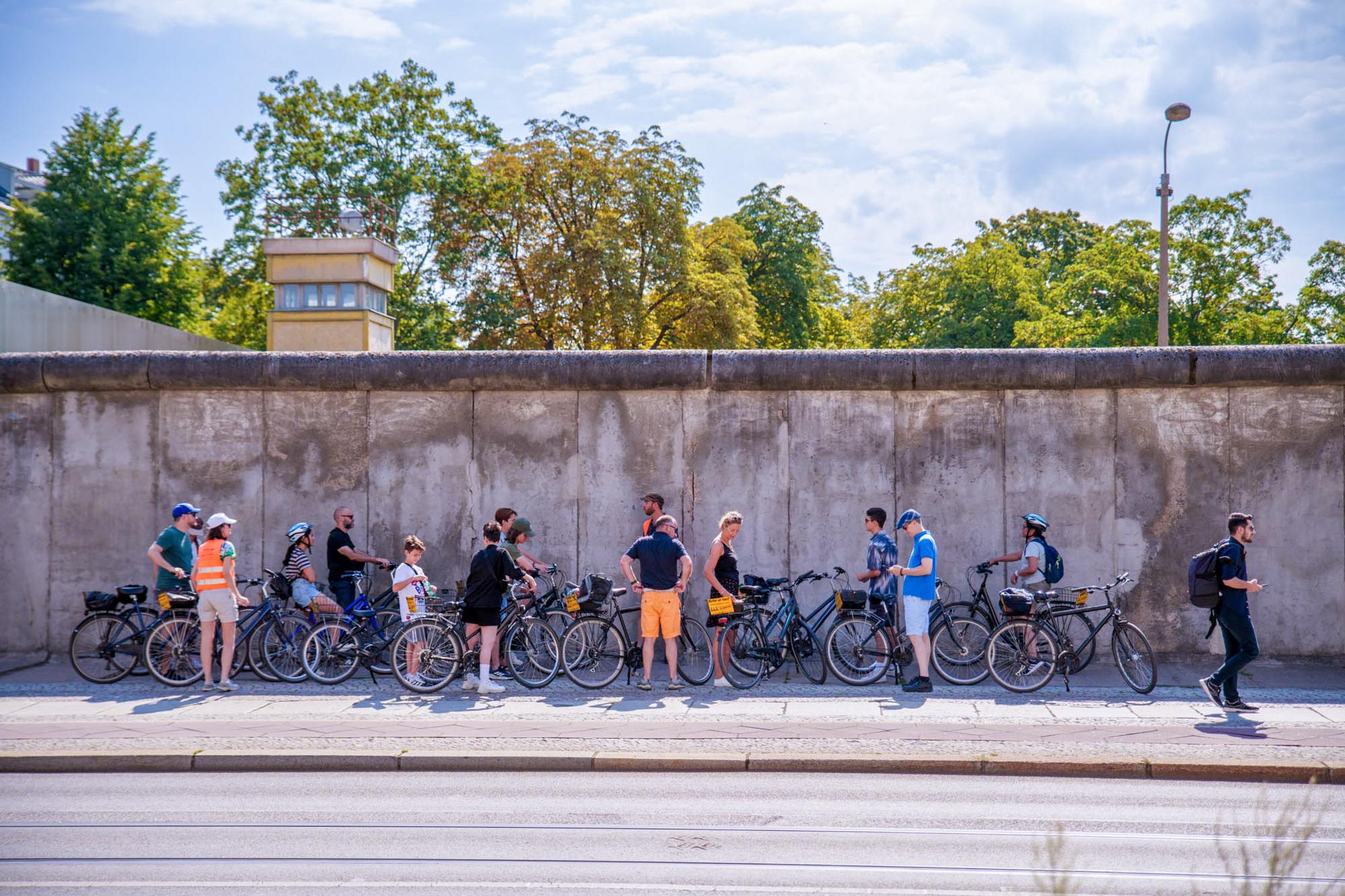 Die ehemalige Berliner Mauer mit Fahrrädern und Fahrradfahrern davor.