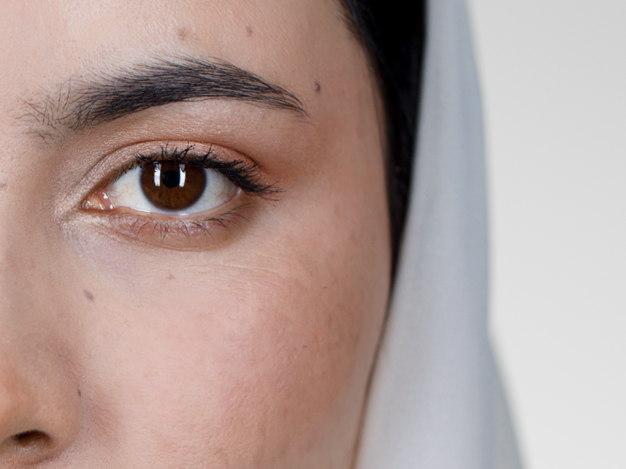 Das Auge einer Frau mit Hijab. Das weiße Kopftuch ist im Hintergrund zu sehen.