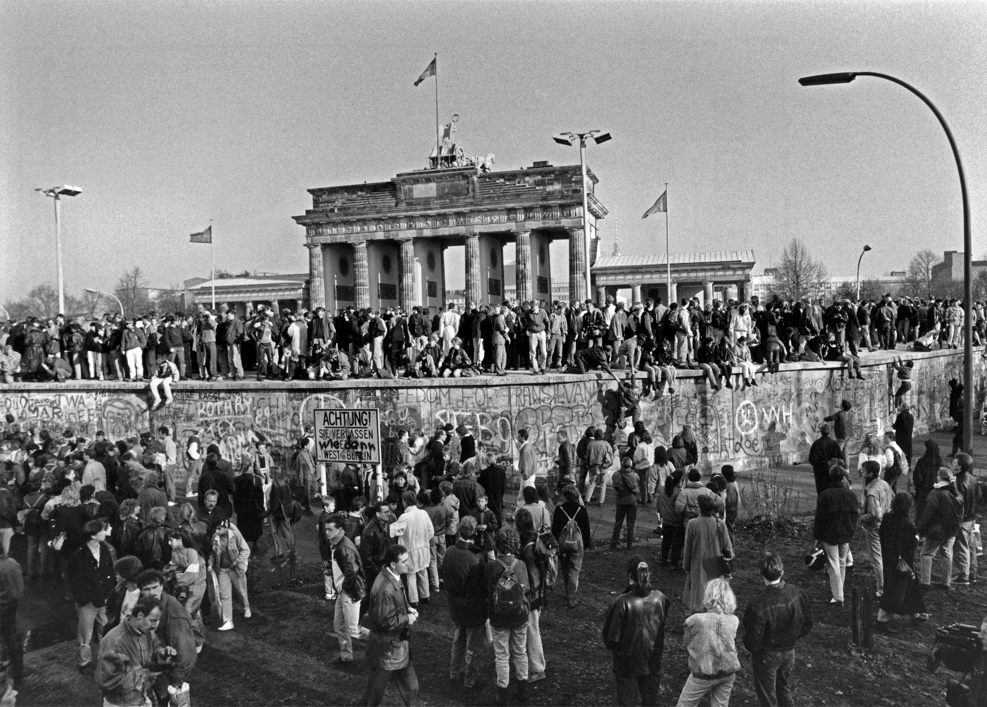 Ein Schwarzweiß-Foto der Berliner Mauer mit Menschenmassen beim Mauerfall.