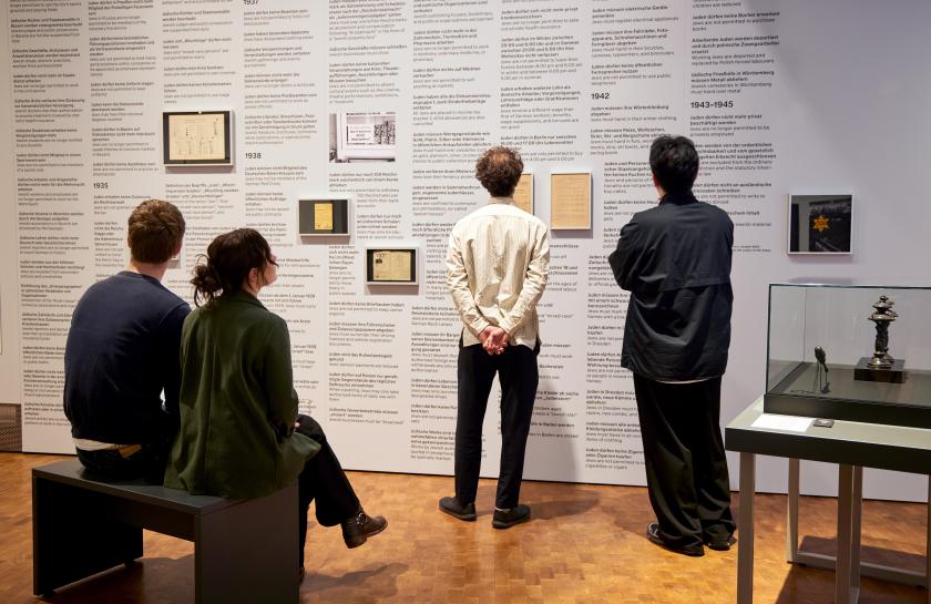 Menschen stehen in einer Ausstellung vor einer Wand mit Text
