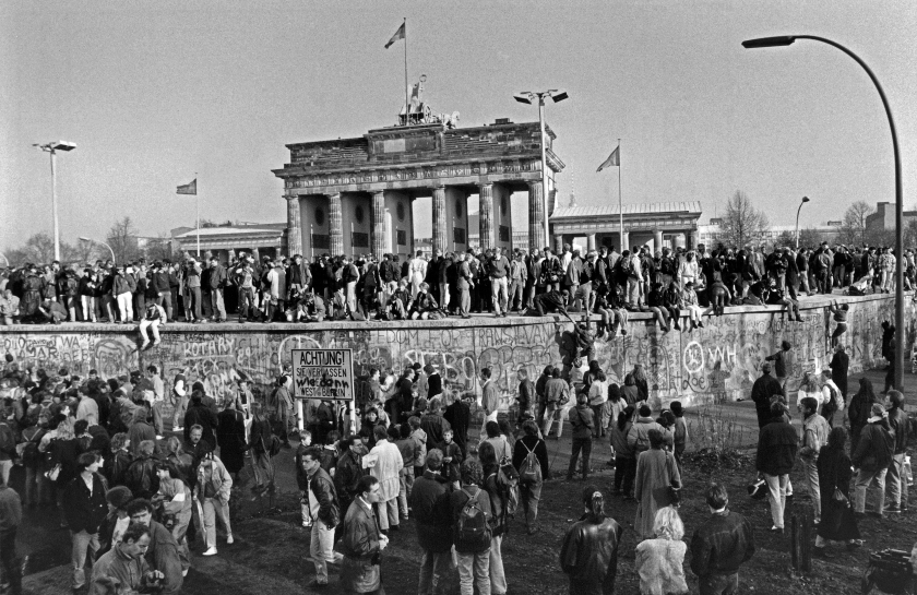 Ein Schwarzweiß-Foto der Berliner Mauer mit Menschenmassen beim Mauerfall.