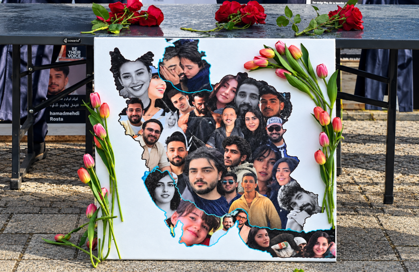 Ein Foto eines Protestschildes mit den Fotos von iranischen Menschen und Blumen darauf.